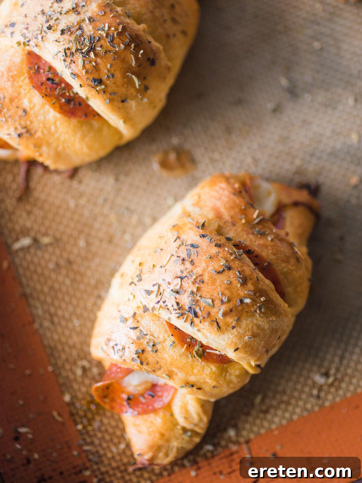 Freshly baked pepperoni rolls cooling on a silpat-lined baking sheet, golden and bubbly