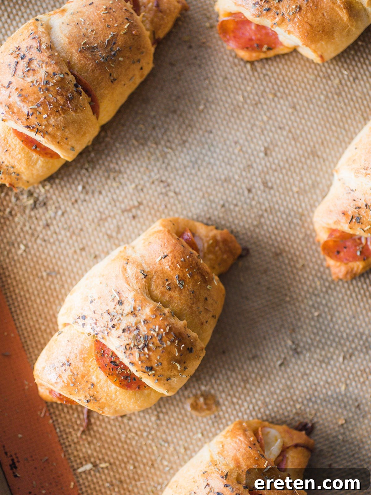 Close-up shot of a single baked pepperoni roll, showing its golden crust and delicious filling, on a silicone mat
