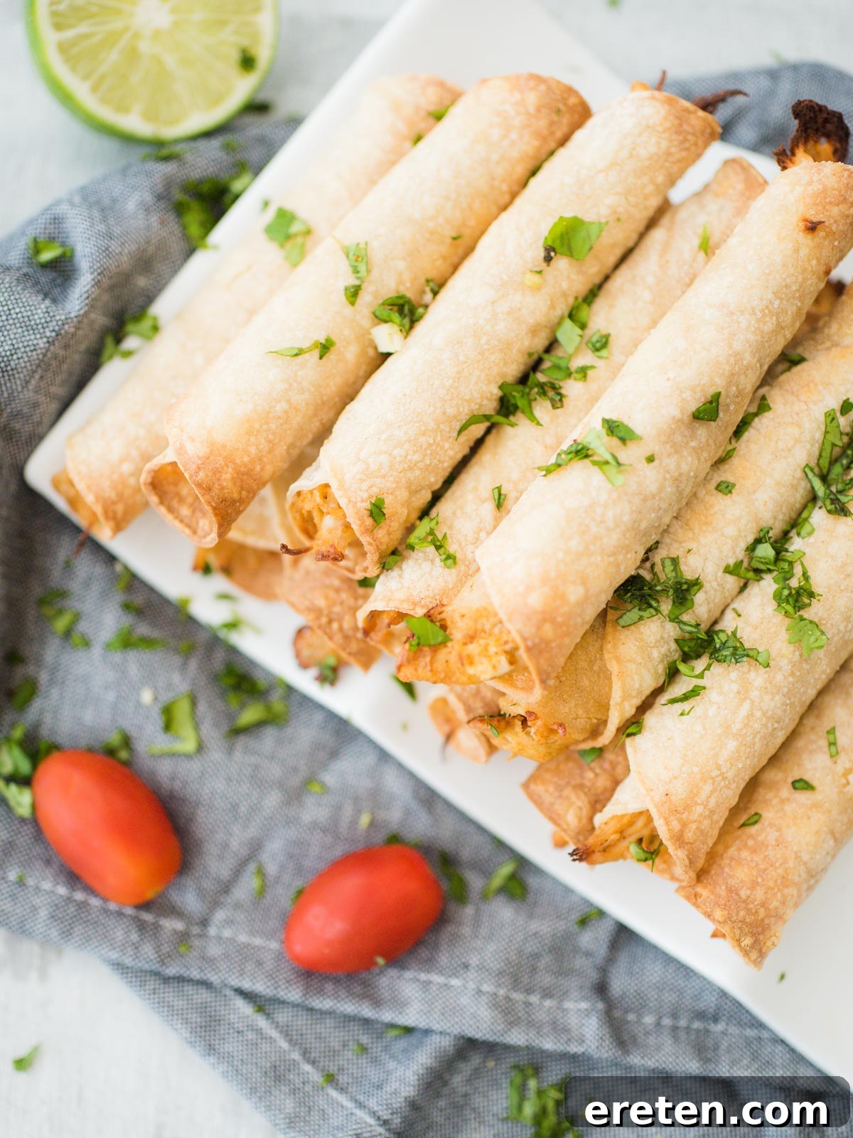 Crispy Creamy Chicken Taquitos 2 Stack of golden-brown crispy baked chicken taquitos on a white plate, garnished with fresh cilantro and a lime wedge, ready to be served.