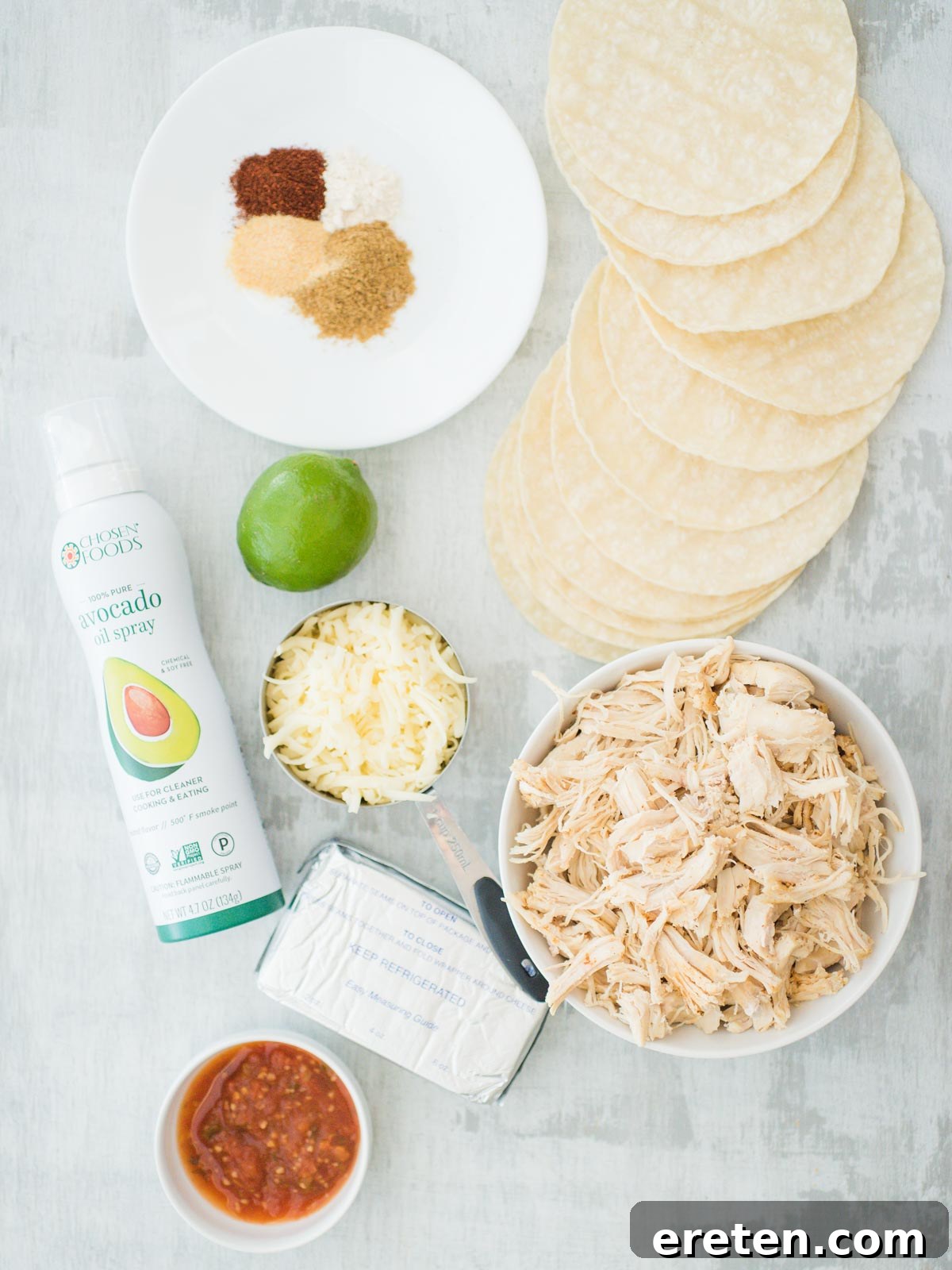 Crispy Creamy Chicken Taquitos 3 Ingredients for making creamy baked chicken taquitos laid out on a kitchen counter: cream cheese, salsa, fresh lime, cumin, chili powder, garlic powder, onion powder, cooked shredded chicken, pepper jack cheese, corn tortillas, and avocado oil spray.
