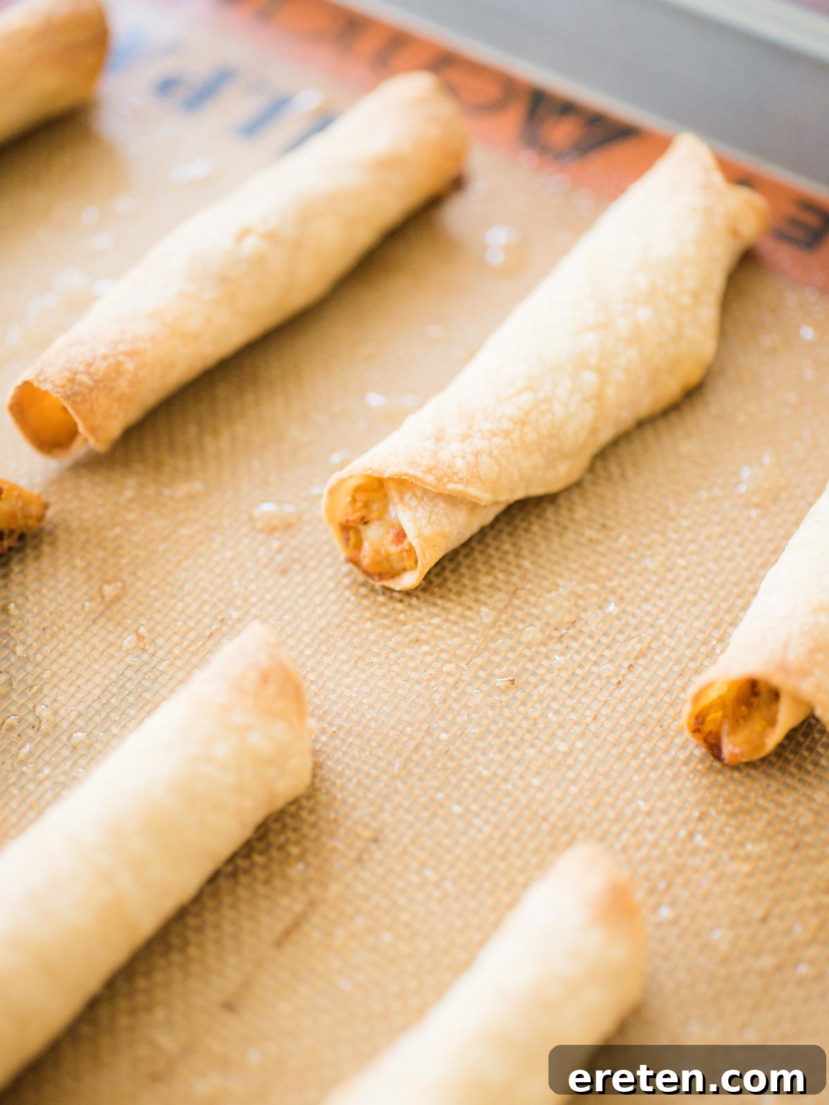 Crispy Creamy Chicken Taquitos 6 Chicken taquitos arranged neatly on a silicone-lined baking sheet, lightly sprayed with oil, and ready to go into the oven for baking to a golden, crispy finish.