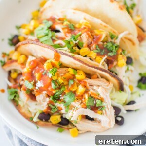 A white shallow bowl with tacos stuffed with bbq chicken, beans, corn, and cilantro
