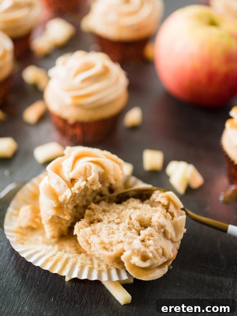 Caramel Apple Cinnamon Cupcakes 5 A perfectly baked and frosted apple cider cupcake, split in half to reveal its moist interior, resting in a gold and white liner with a small fork.
