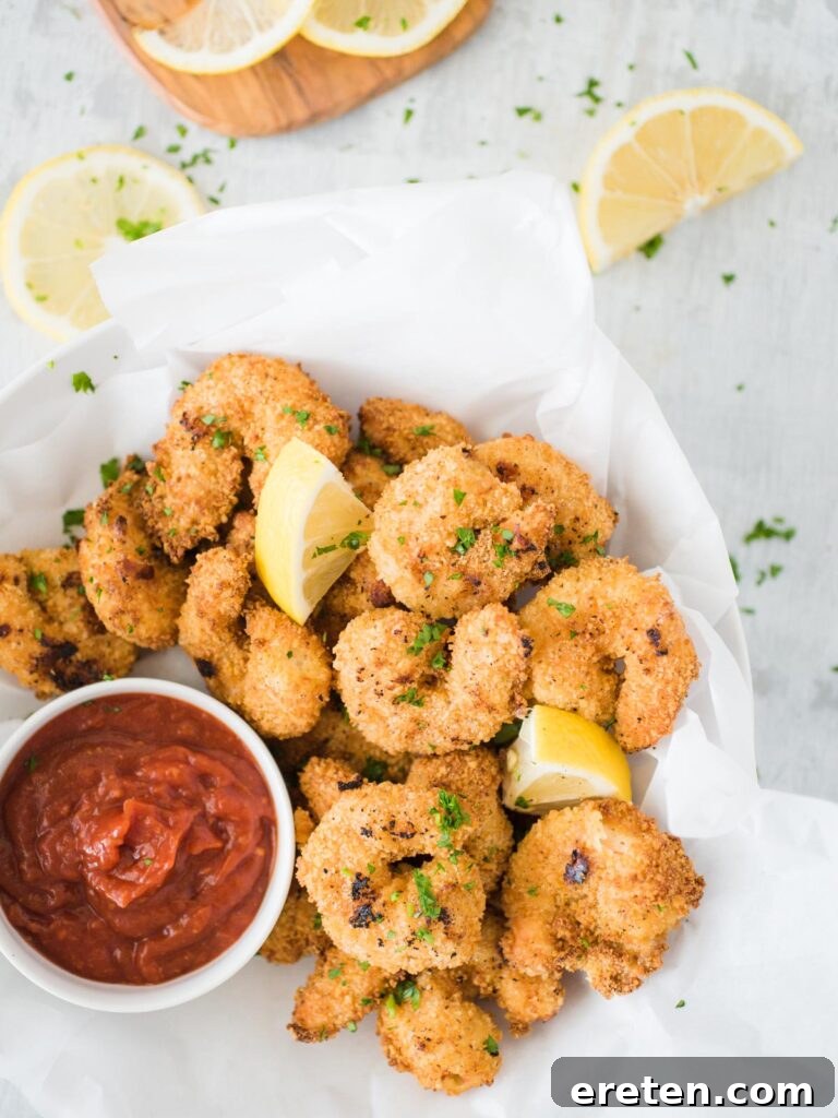 A bowl of crispy air fried popcorn shrimp with dipping sauce and lemon wedges, ready to be served.