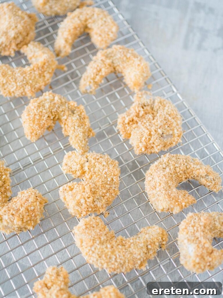 Breaded raw shrimp neatly arranged on a cooling rack, prepared for air frying.