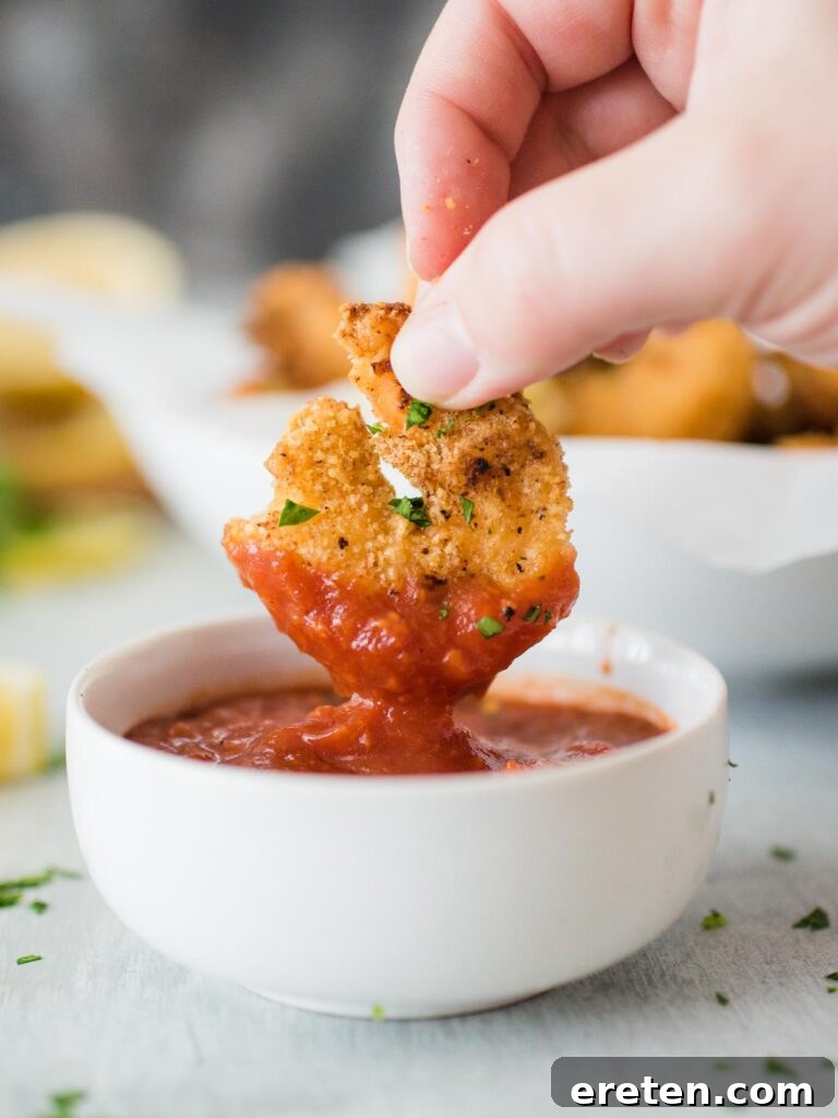 Close-up of a crispy air fried shrimp being dipped into a small bowl of cocktail sauce.