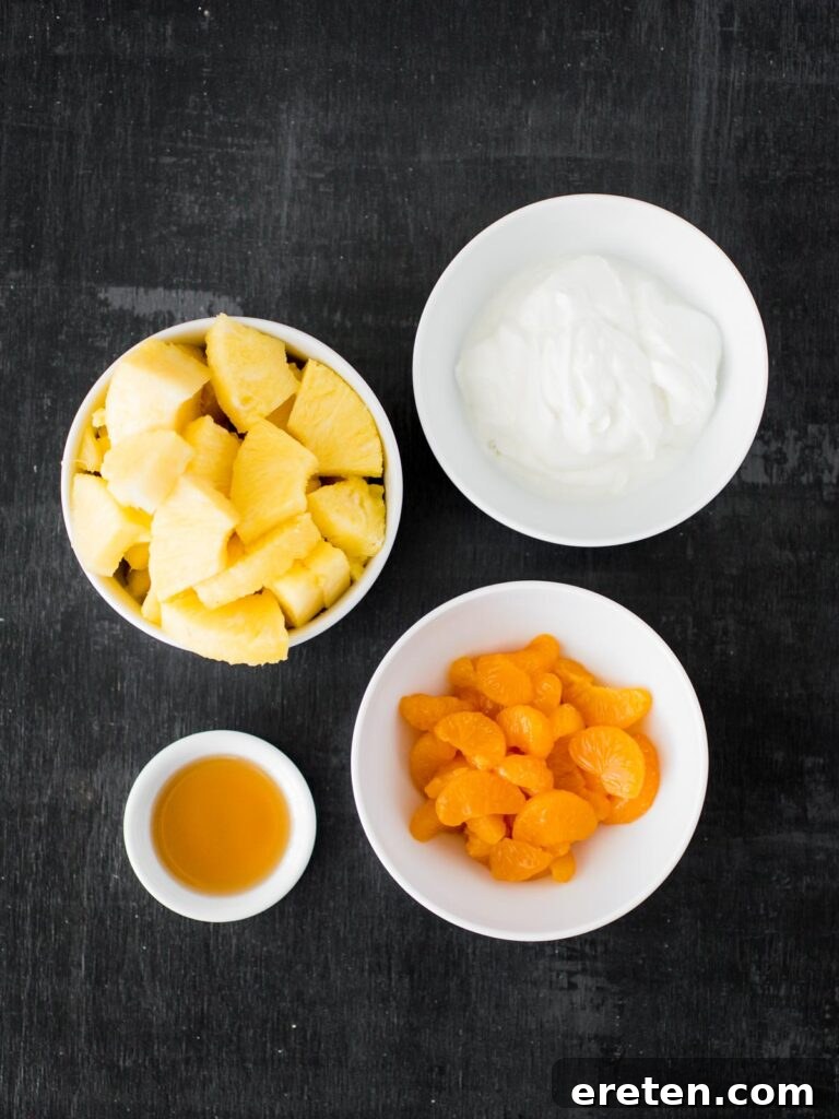Ingredients laid out for Candy Corn Inspired Fruit Parfait, including plain Greek yogurt, maple syrup, pineapple chunks, and mandarin oranges