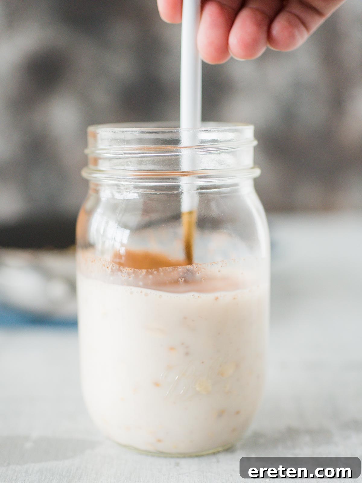 A spoon stirring the apple pie overnight oats mixture in a jar