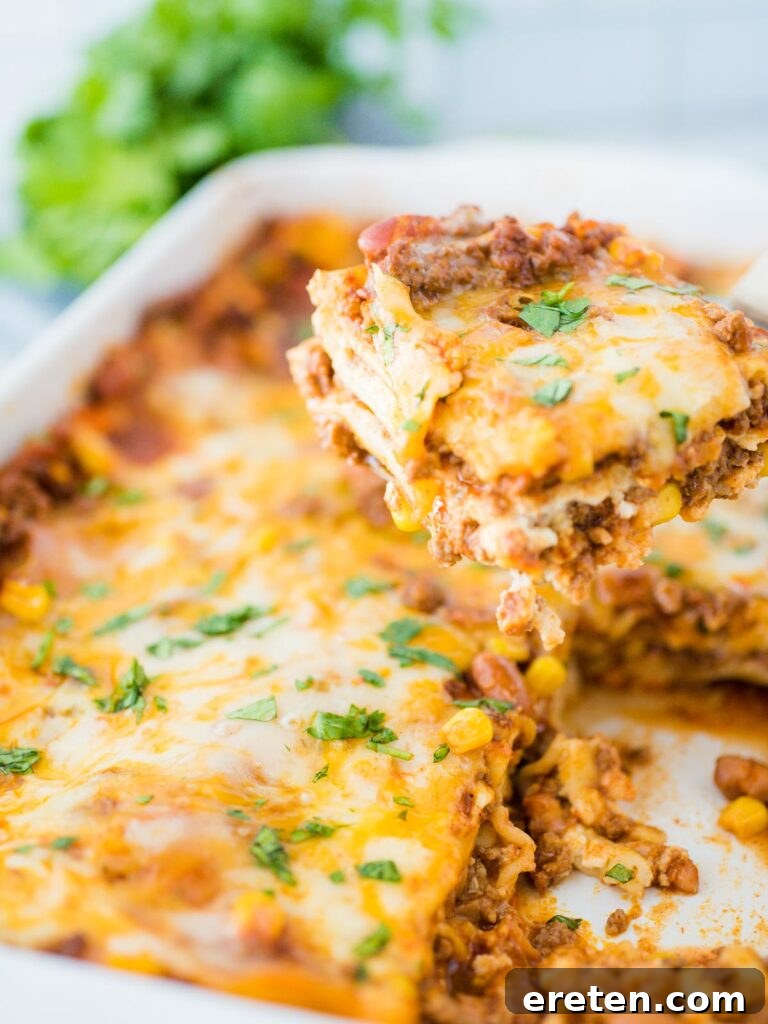 Kickin Tex Mex Lasagna 2 A generous scoop of Tex Mex lasagna being lifted from a baking dish, revealing its vibrant layers of pasta, meat, beans, and melted cheese.