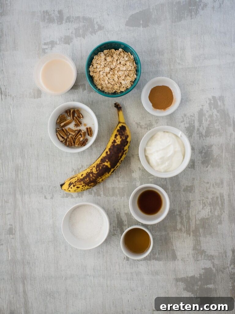 Creamy Banana Nut Bread Overnight Oats 3 A collection of fresh ingredients laid out, including old-fashioned oats, cinnamon, kosher salt, pecans, a ripe banana, Greek yogurt, maple syrup, vanilla extract, and almond milk, ready for making banana bread overnight oats.