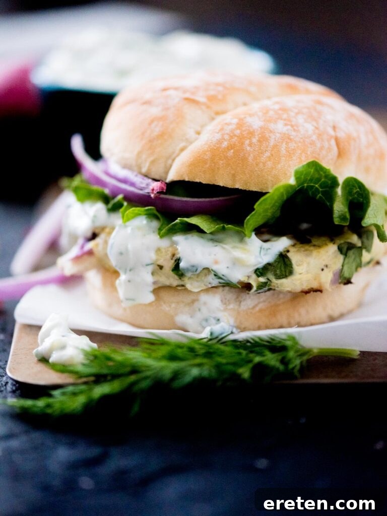 A perfectly grilled Greek turkey burger nestled in a bun, topped with a dollop of creamy tzatziki sauce, fresh red onion, and crisp lettuce leaves, ready to be enjoyed.