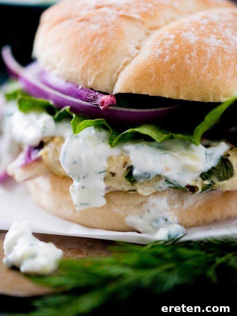 A perfectly grilled Greek turkey burger in a bun, generously topped with cool tzatziki sauce, thinly sliced red onion, and crisp lettuce, showcasing its delicious appeal.