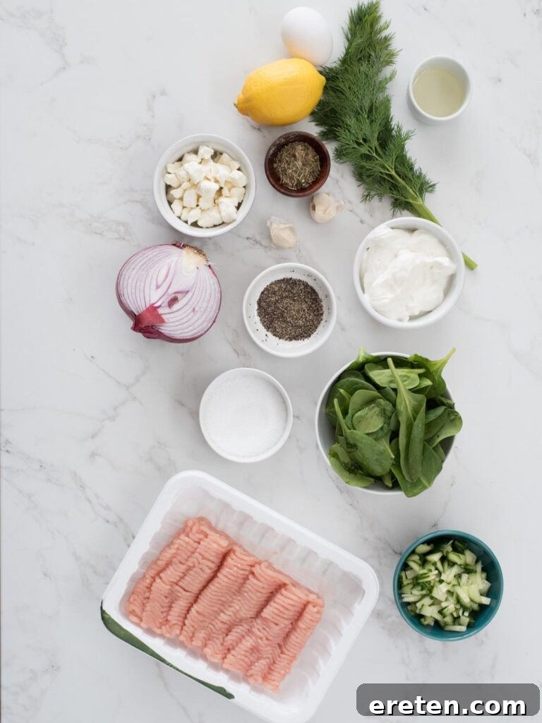 A vibrant selection of ingredients laid out, including ground turkey, fresh spinach, crumbled feta, red onion, garlic, eggs, and a jar of Greek seasoning, ready to be combined for making Greek turkey burgers. Also present are ingredients for tzatziki: Greek yogurt, English cucumber, lemon, fresh dill, and olive oil.