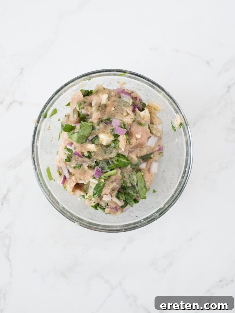 The Greek turkey burger ingredients, including ground turkey, feta, spinach, and red onion, perfectly mixed together in a bowl, ready for patty formation.