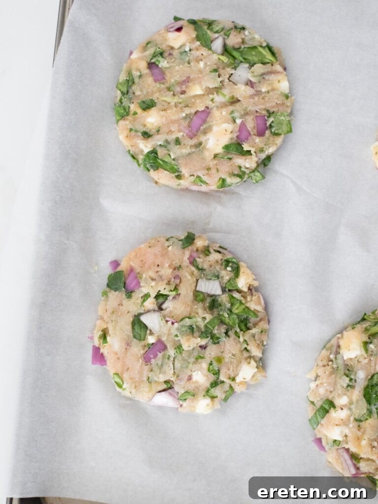Four perfectly formed raw turkey burger patties arranged neatly on parchment paper, awaiting their turn on the grill.