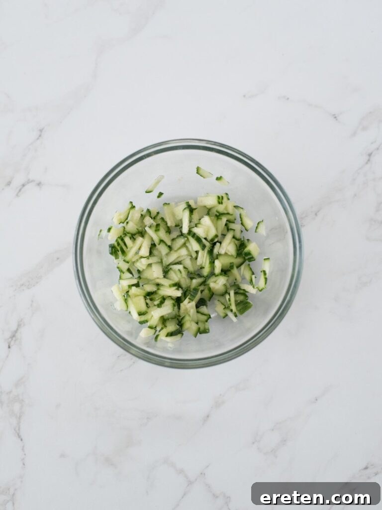 Freshly chopped cucumbers mixed with kosher salt in a bowl, a crucial step for preparing crisp, non-watery tzatziki sauce.