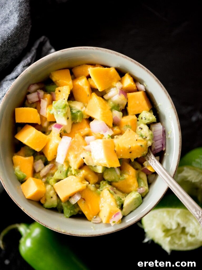 A beautiful bowl of freshly made avocado mango salsa, being scooped with a spoon.