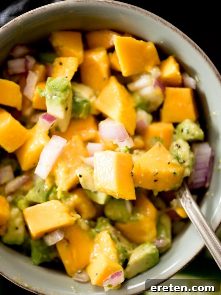 Close-up of a serving of avocado mango salsa in a bowl, with a spoon scooping some out.
