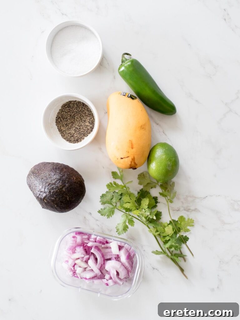 Fresh ingredients laid out for making avocado mango salsa: mangoes, avocado, jalapeno, red onion, cilantro, and limes.