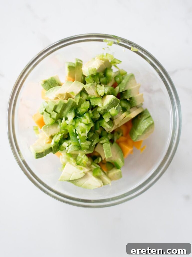 Finely chopped jalapeno being added to the mixing bowl with mango and avocado.