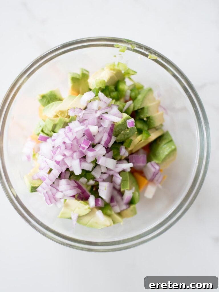 Diced red onion joining the other ingredients in the mixing bowl for the salsa.