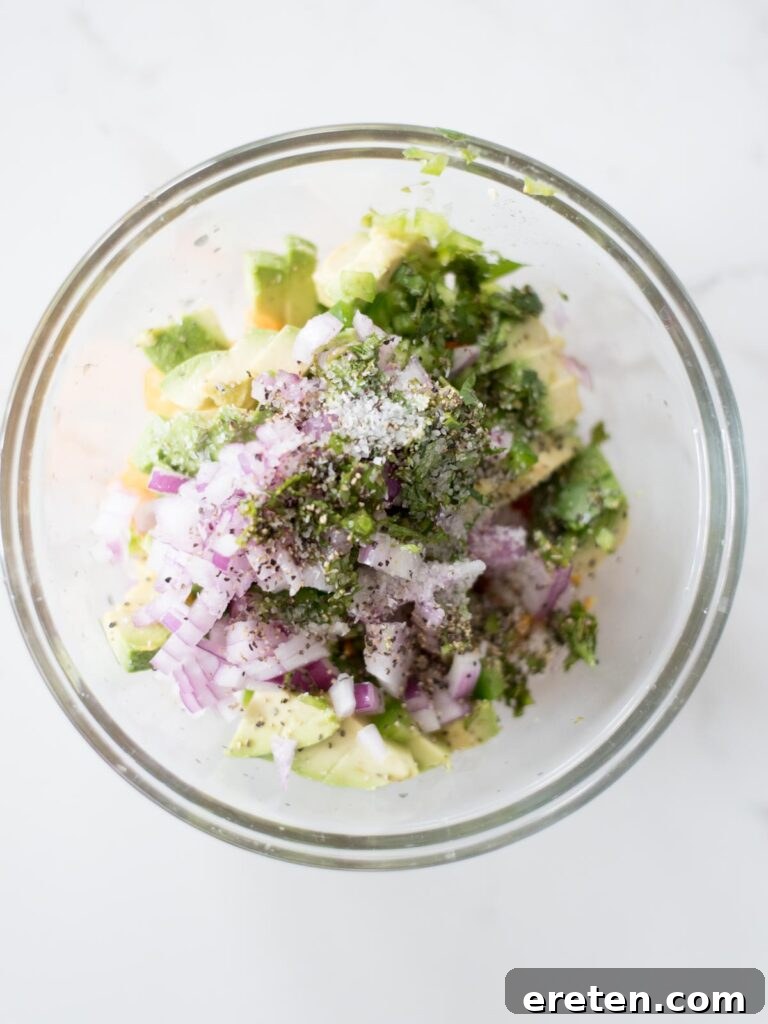 All unmixed ingredients for avocado mango salsa in a clear mixing bowl, before stirring.