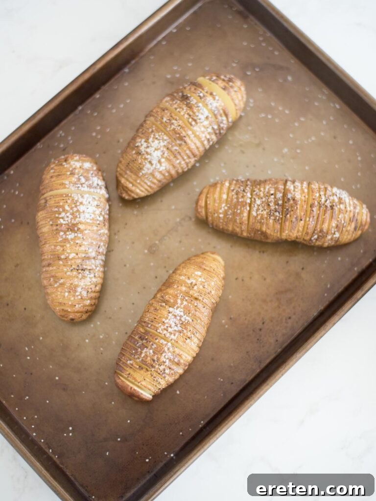 partially baked hasselback potatoes on a baking sheet, beginning to fan out