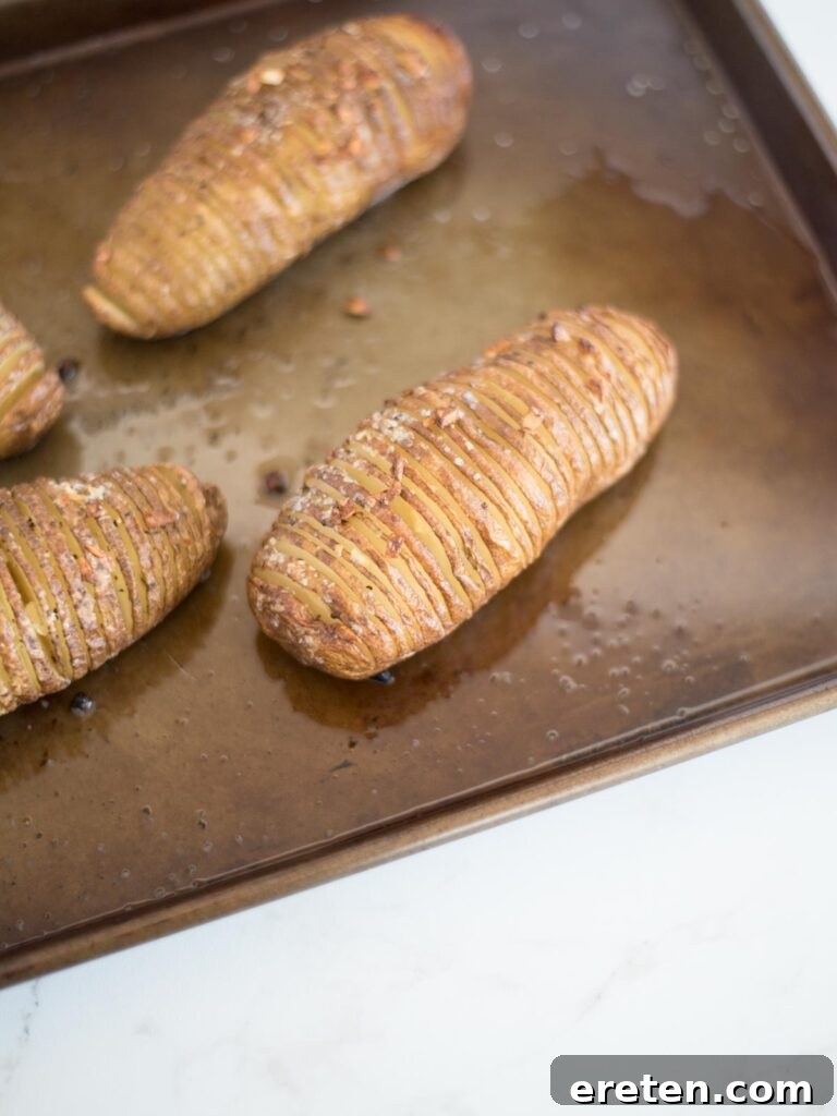 hasselback potato cooked halfway through, showing fanned slices on a baking sheet, ready for final baking