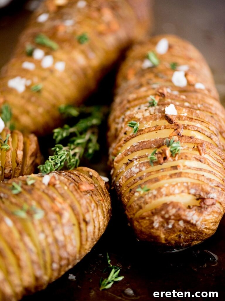 close-up of finished garlic butter hasselback potatoes, garnished with fresh thyme and a sprinkle of flaked salt