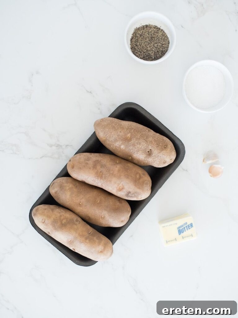 ingredients for garlic hasselback potatoes, including fresh potatoes, butter, garlic, salt, pepper, and thyme