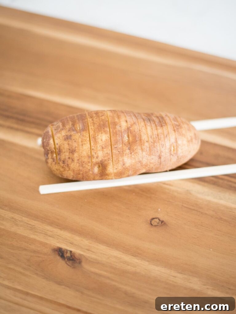 sliced hasselback potato resting on chopsticks, showcasing the even cuts achieved