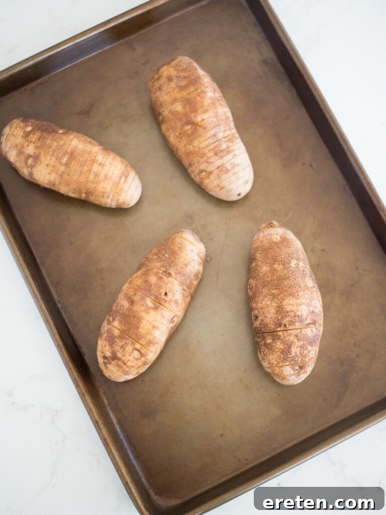 several sliced hasselback potatoes neatly arranged on a baking sheet before baking