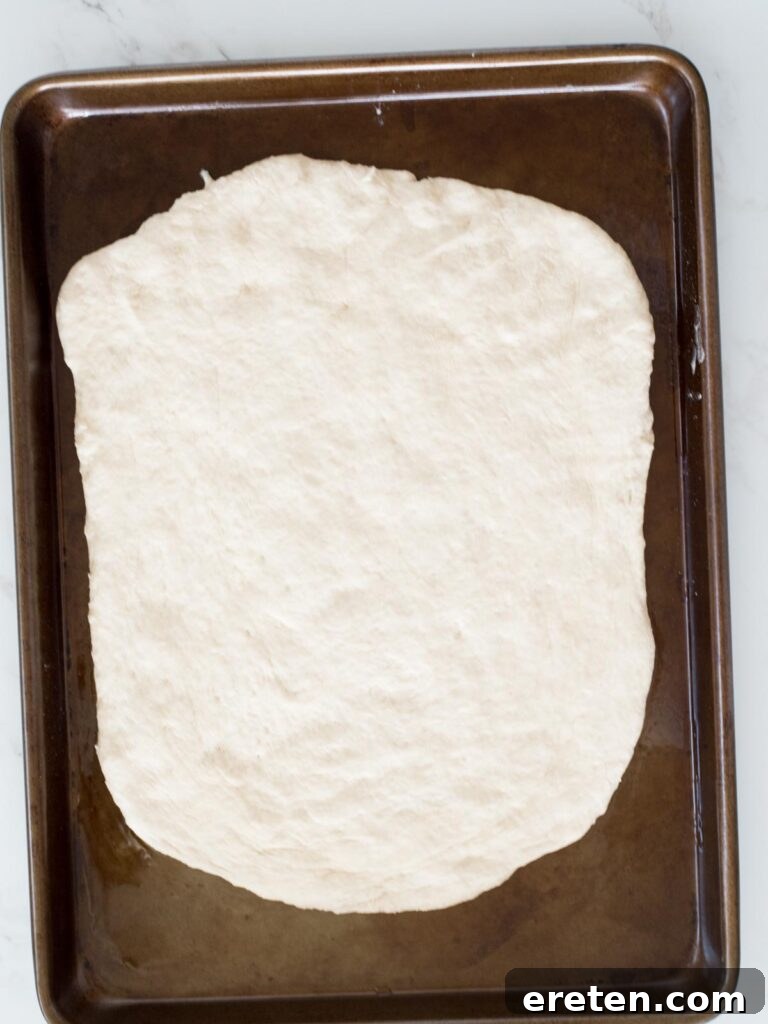 bread dough spread out on an oiled baking sheet