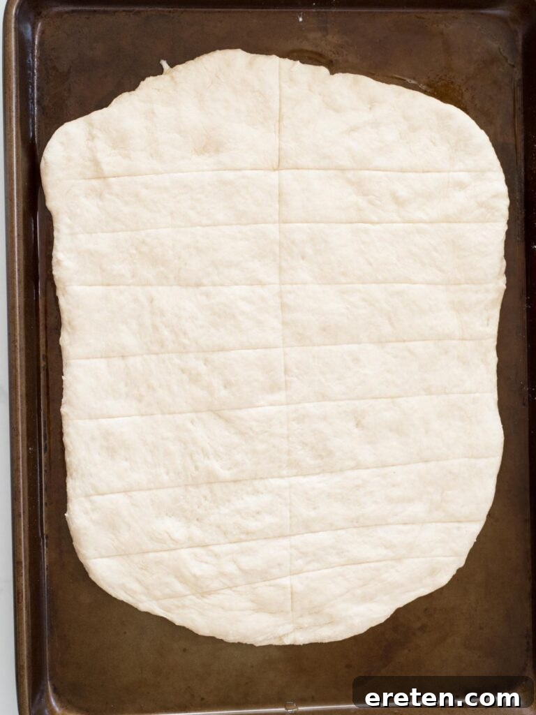 scored bread dough on a baking sheet, ready to rise