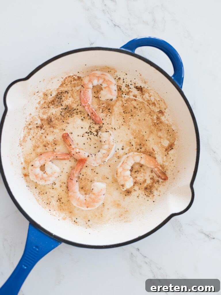 Shrimp cooking to a perfect pink in a blue enamel cast iron skillet, seasoned with salt and pepper.