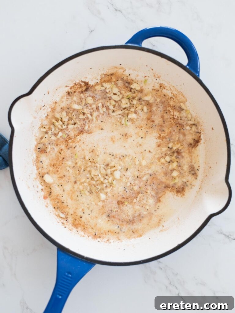 Minced garlic being gently sautéed in melted butter within an enameled cast iron skillet, releasing its fragrant aroma.
