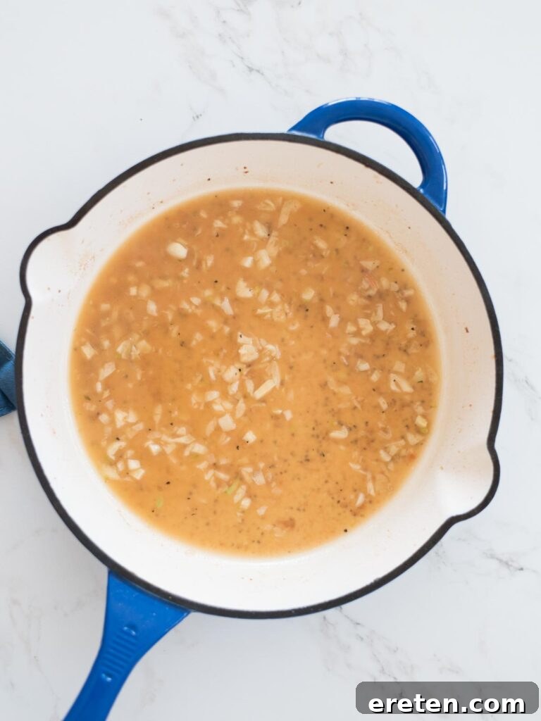 Chicken broth being poured into a skillet to deglaze the pan, incorporating all the rich flavors from the bottom.