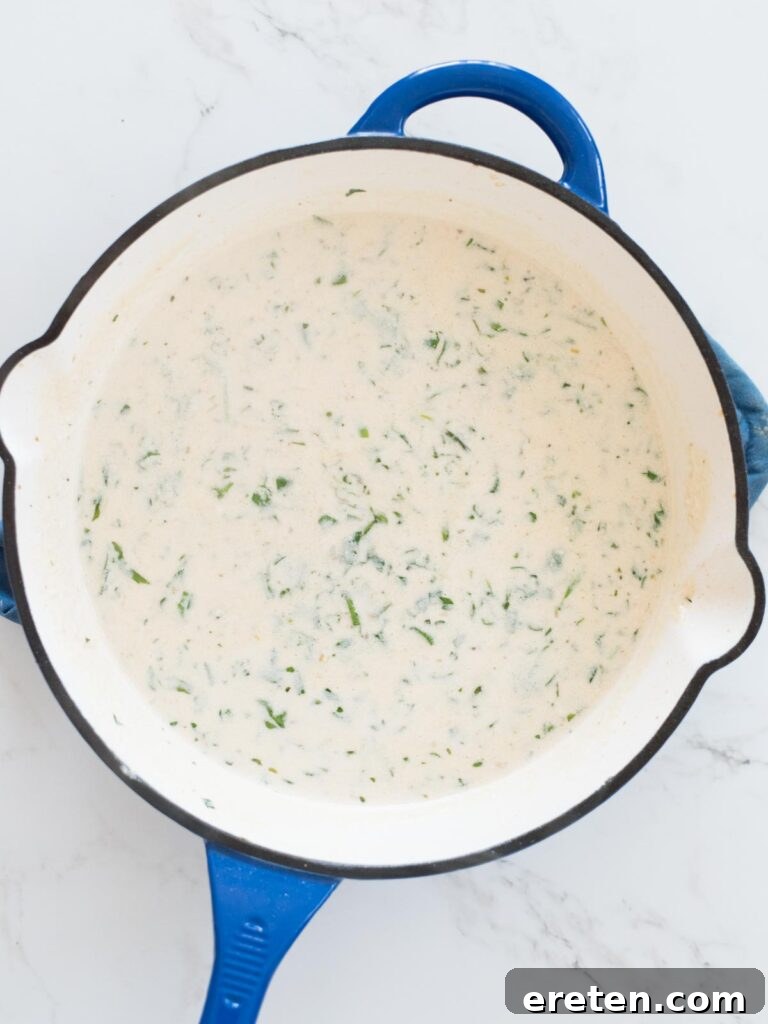 Half and half being added to the skillet, mixing with the broth and garlic to form the creamy sauce base.