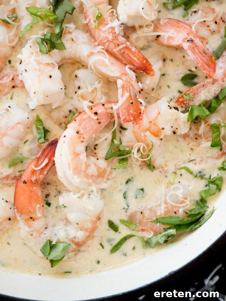 A close-up shot of creamy garlic shrimp with parmesan, perfectly cooked and glistening in a blue enamel cast iron skillet, garnished with fresh herbs.