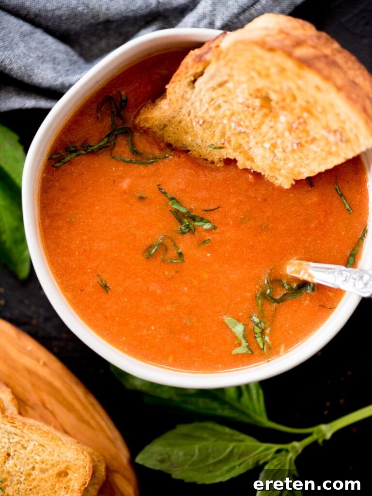 Comforting Roasted Tomato Basil Soup 2 Roasted tomato basil soup in a bowl topped with fresh basil and a grilled cheese sandwich dipped in