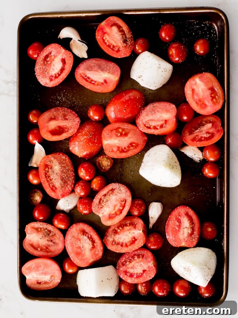 Comforting Roasted Tomato Basil Soup 4 Roma tomatoes, cherry tomatoes, garlic, and onion arranged on a sheet pan with olive oil, salt, and pepper