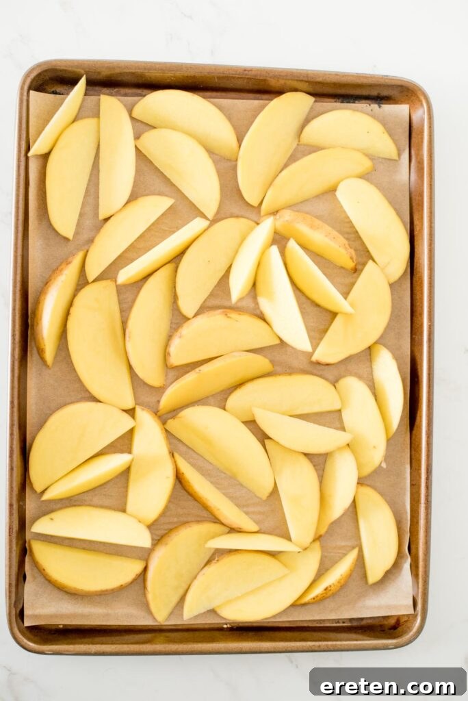 Raw potato wedges cut and arranged on a parchment-lined baking sheet before seasoning.
