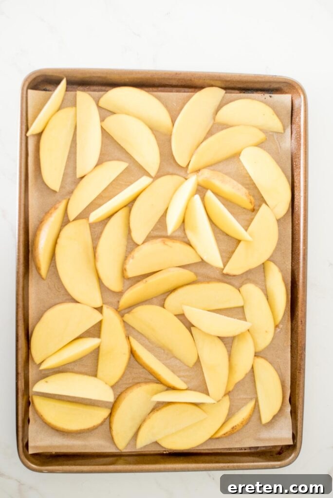 Close-up of potato wedges on a baking sheet, lightly sprayed with avocado oil.