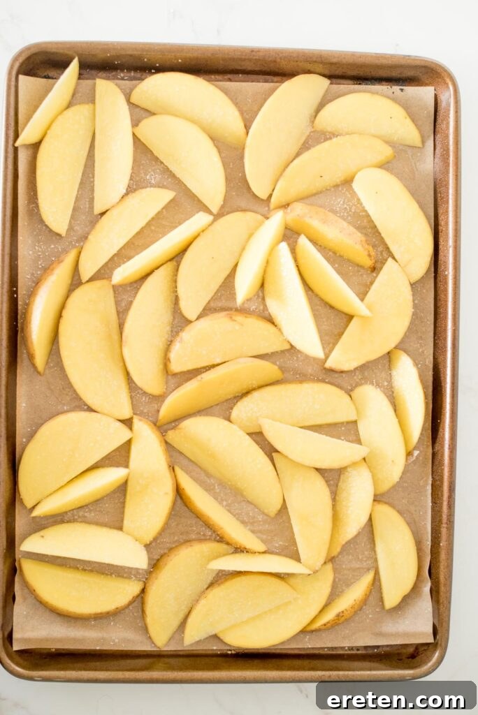 Potato wedges on a baking sheet, seasoned with coarse salt, before baking.