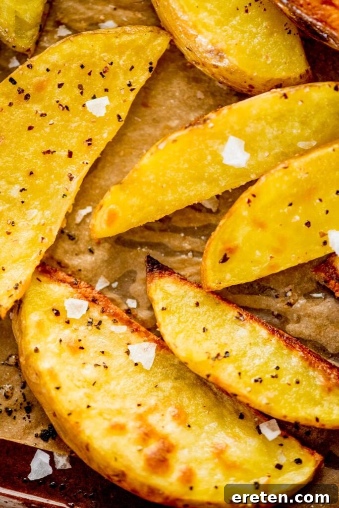 Crispy oven baked garlic potato wedges with flaky sea salt, served on a baking sheet, ready for dipping.