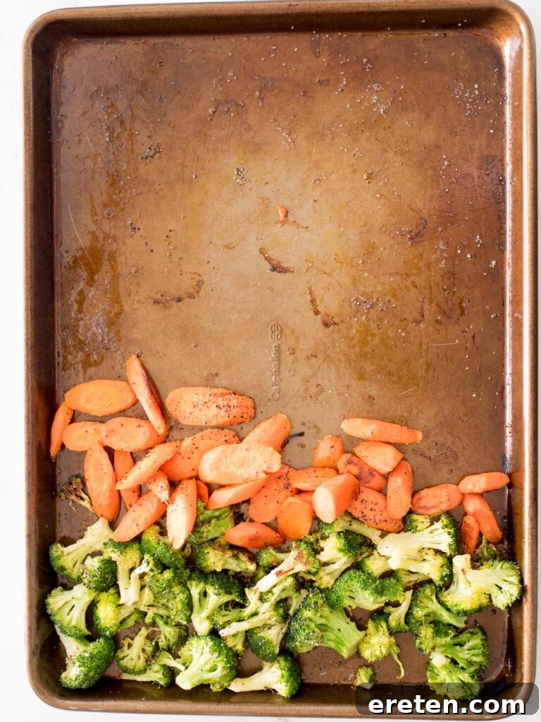 sheet pan with partially roasted broccoli and carrots moved to one side