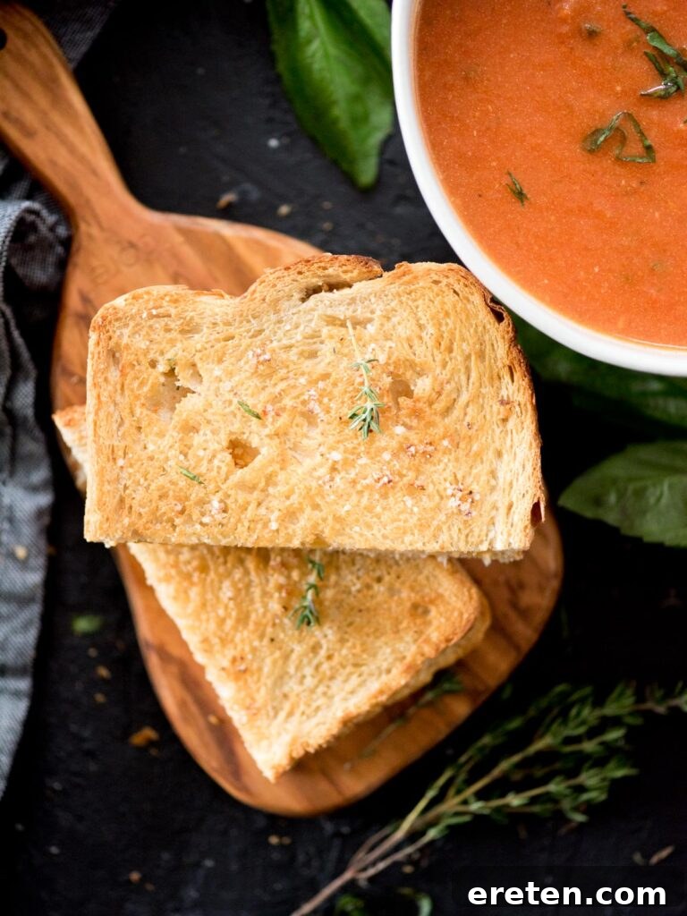 Air Fryer Grilled Cheese Perfection 2 Air fried grilled cheese sandwich cut in half, showcasing its golden crust and melted cheese, served alongside a warm bowl of tomato basil soup and garnished with a sprig of fresh thyme.