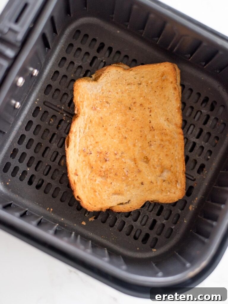 Air Fryer Grilled Cheese Perfection 9 A perfectly cooked grilled cheese sandwich, golden brown and crispy, resting inside an air fryer basket after its cooking cycle.