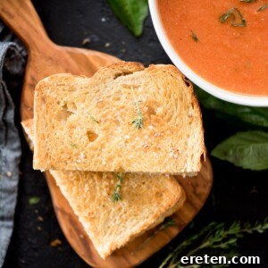 Air fried grilled cheese sandwich sliced in half on a cutting board next to a bowl of soup and topped with a sprig of fresh thyme, showcasing its crispy exterior and melted interior.