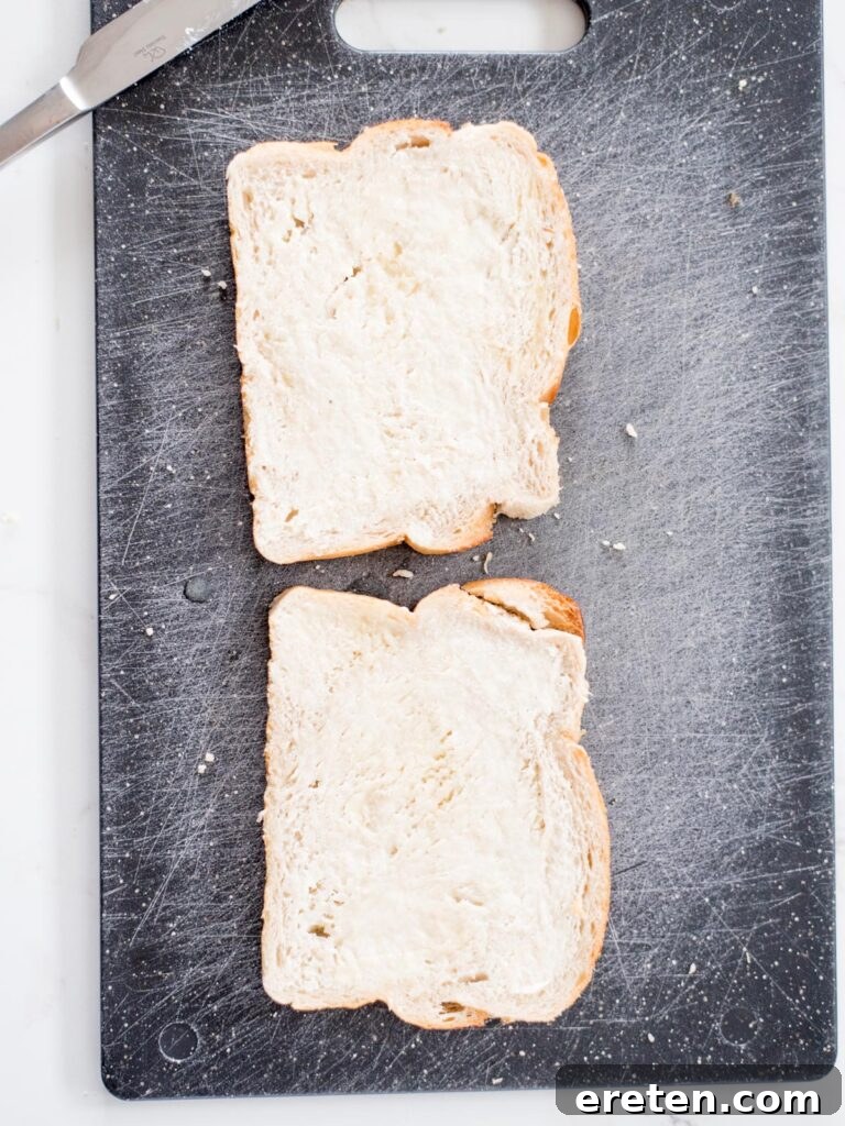 Air Fryer Grilled Cheese Perfection 4 Two slices of bread evenly buttered on one side, laid out on a clean cutting board, ready for seasoning and assembly.